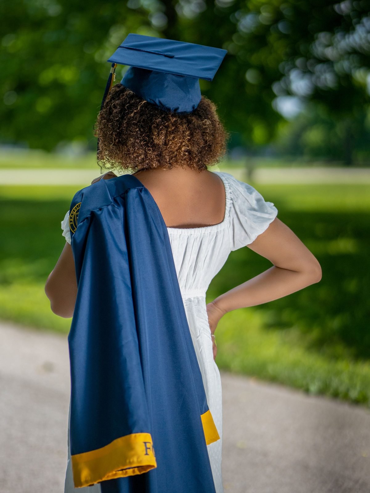 A graduate in cap and gown seen from behind in a sunny park