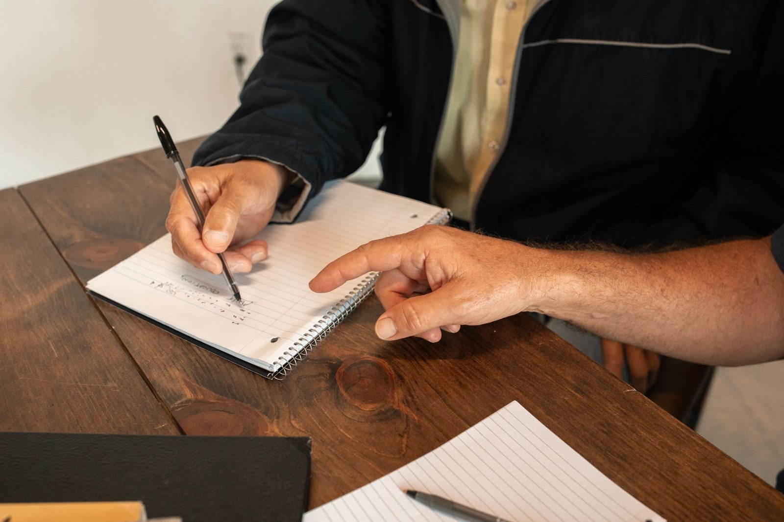 A tutor points to a line in a learner's notebook as they write